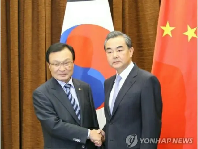 握手を交わす李特使（左）と王外相（共同取材団）＝１８日、北京（聯合ニュース）
