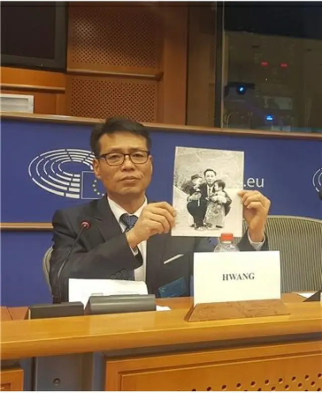 欧州議会人権小委員会の公聴会に出席した被害者家族会のファン・インチョル代表。拉致された父親と幼いころに写した写真を見せながら、生死確認と送還を訴えた＝5日、ブリュッセル（聯合ニュース）