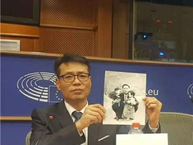欧州議会人権小委員会の公聴会に出席した被害者家族会のファン・インチョル代表。拉致された父親と幼いころに写した写真を見せながら、生死確認と送還を訴えた＝5日、ブリュッセル（聯合ニュース）