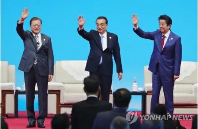 ビジネスサミットの会場で手を振る文大統領（左）、李首相（中央）、安倍首相（右）＝24日、成都（聯合ニュース）