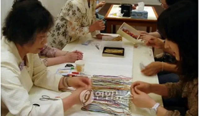 日本人の工芸家から組みひもの作り方を習う観光客＝１８日、ソウル（聯合ニュース）