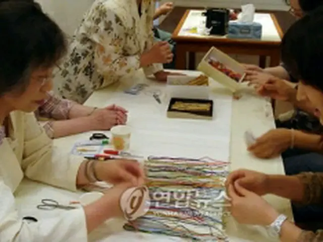 日本人の工芸家から組みひもの作り方を習う観光客＝１８日、ソウル（聯合ニュース）