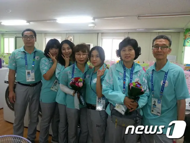 洗濯場で働くボランティアが北朝鮮の女子サッカー選手から貰った花束を持ち記念写真を撮っている（提供:news1）