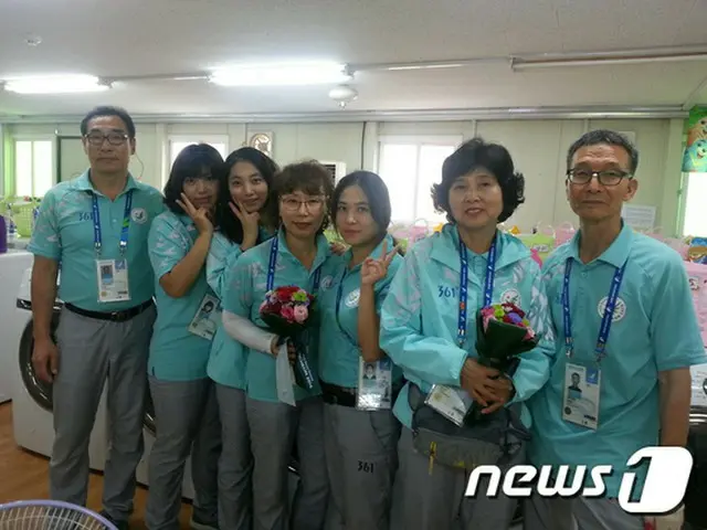 洗濯場で働くボランティアが北朝鮮の女子サッカー選手から貰った花束を持ち記念写真を撮っている（提供:news1）