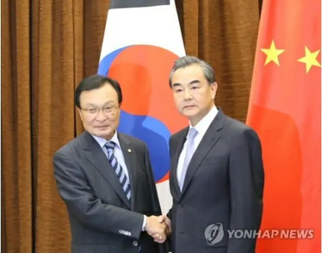 握手を交わす李特使（左）と王外相（共同取材団）＝１８日、北京（聯合ニュース）