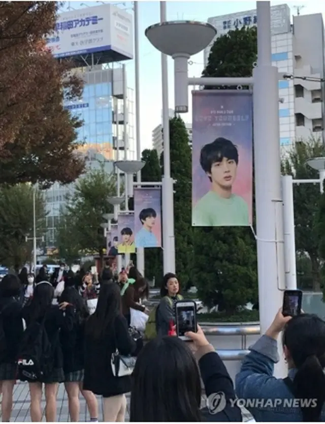 会場周辺に飾られたＢＴＳメンバーの写真を撮影するファン＝１４日、東京（聯合ニュース）
