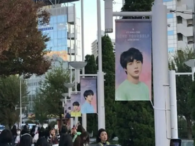 会場周辺に飾られたＢＴＳメンバーの写真を撮影するファン＝１４日、東京（聯合ニュース）