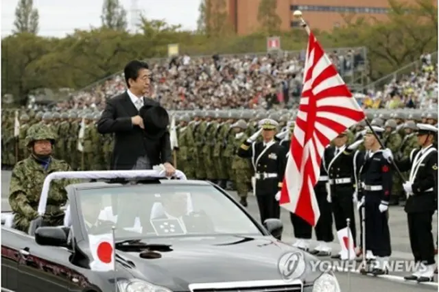 ２０１８年１０月に行われた陸上自衛隊の行事で敬礼を受ける安倍首相（中央）と旭日旗を持った自衛隊員（資料写真）＝（共同＝聯合ニュース）