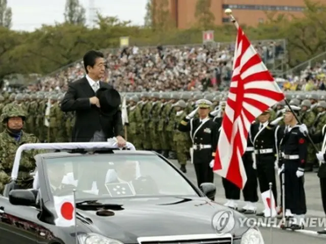 ２０１８年１０月に行われた陸上自衛隊の行事で敬礼を受ける安倍首相（中央）と旭日旗を持った自衛隊員（資料写真）＝（共同＝聯合ニュース）