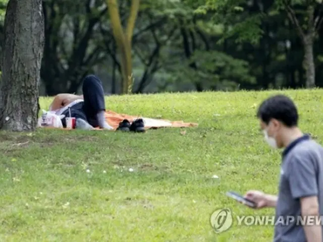 蒸し暑い日となった２日、ソウルの汝矣島公園の木陰で横になる市民＝（聯合ニュース）