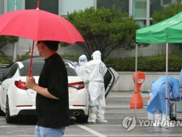 光州市内の駐車場に設けられたドライブスルー型専用診療所で雨の中、検体を採取する医療関係者＝６日、光州（聯合ニュース）