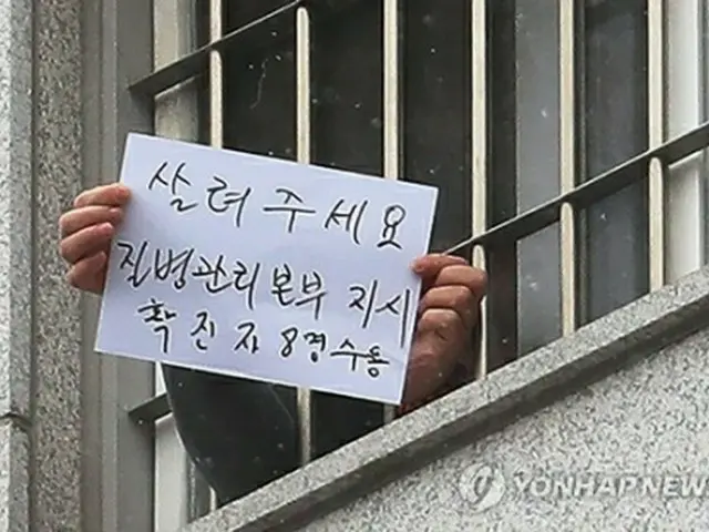 拘置所の収容者が感染防止対策に対する不満を書いた紙を報道陣に示している。１室に感染者８人収容と書かれている＝２９日、ソウル（聯合ニュース）