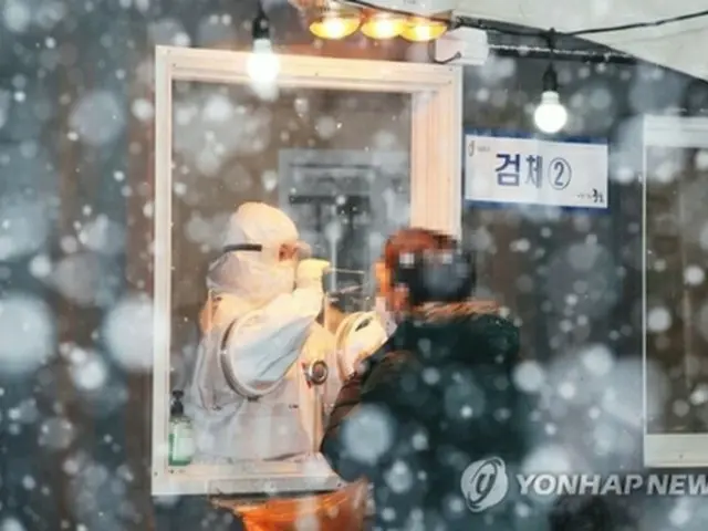 雪が降りしきる中、ソウル駅前の広場の臨時検査所で新型コロナウイルスの検査を受ける市民＝１２日、ソウル（聯合ニュース）