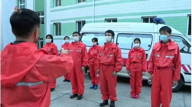 世界各地で新たな変異株「オミクロン株」の感染が広がる中、北朝鮮は防疫を強化しているようだ。救急車の前に並ぶ関係者（朝鮮中央テレビから）＝（聯合ニュース）≪転載・転用禁止≫