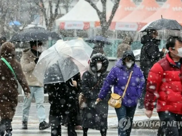 雪が降る中を歩く市民＝１９日、ソウル（聯合ニュース）