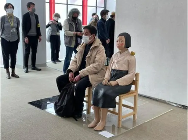 東京・国立で開幕した「表現の不自由展」で、少女像の隣に座る来場客＝２日、東京（聯合ニュース）