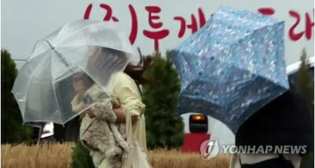 強風と雨の中、傘を差して歩く市民たち＝１１日、ソウル（聯合ニュース）