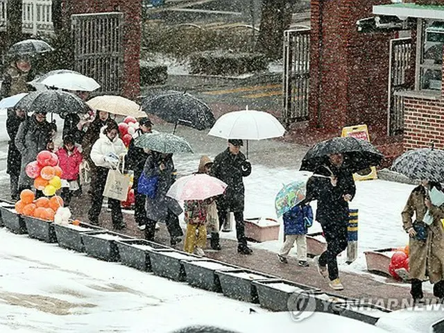 雪の中、傘を差してソウル市内の小学校で行われる入学式に参加する児童と保護者＝４日、ソウル（聯合ニュース）