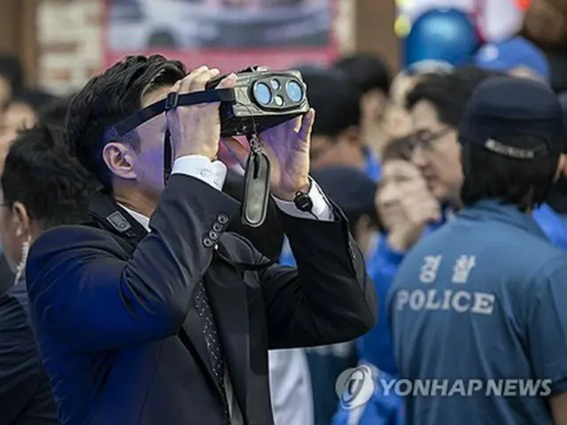 １４日、南部・巨済市で遊説を行う李在明氏を警護する警察官が特殊な双眼鏡で周囲の様子を確認している＝（聯合ニュース）
